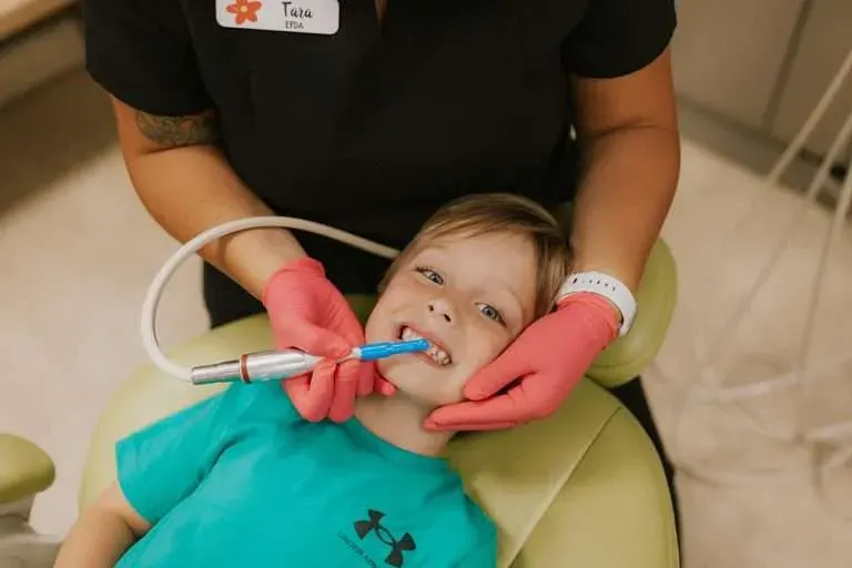 A dental assistant in pink gloves gently cleaning a child's teeth