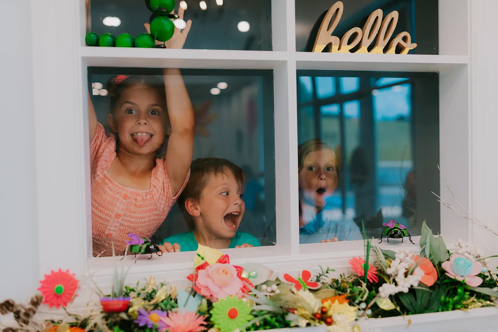 Three kids making happy faces through the playhouse